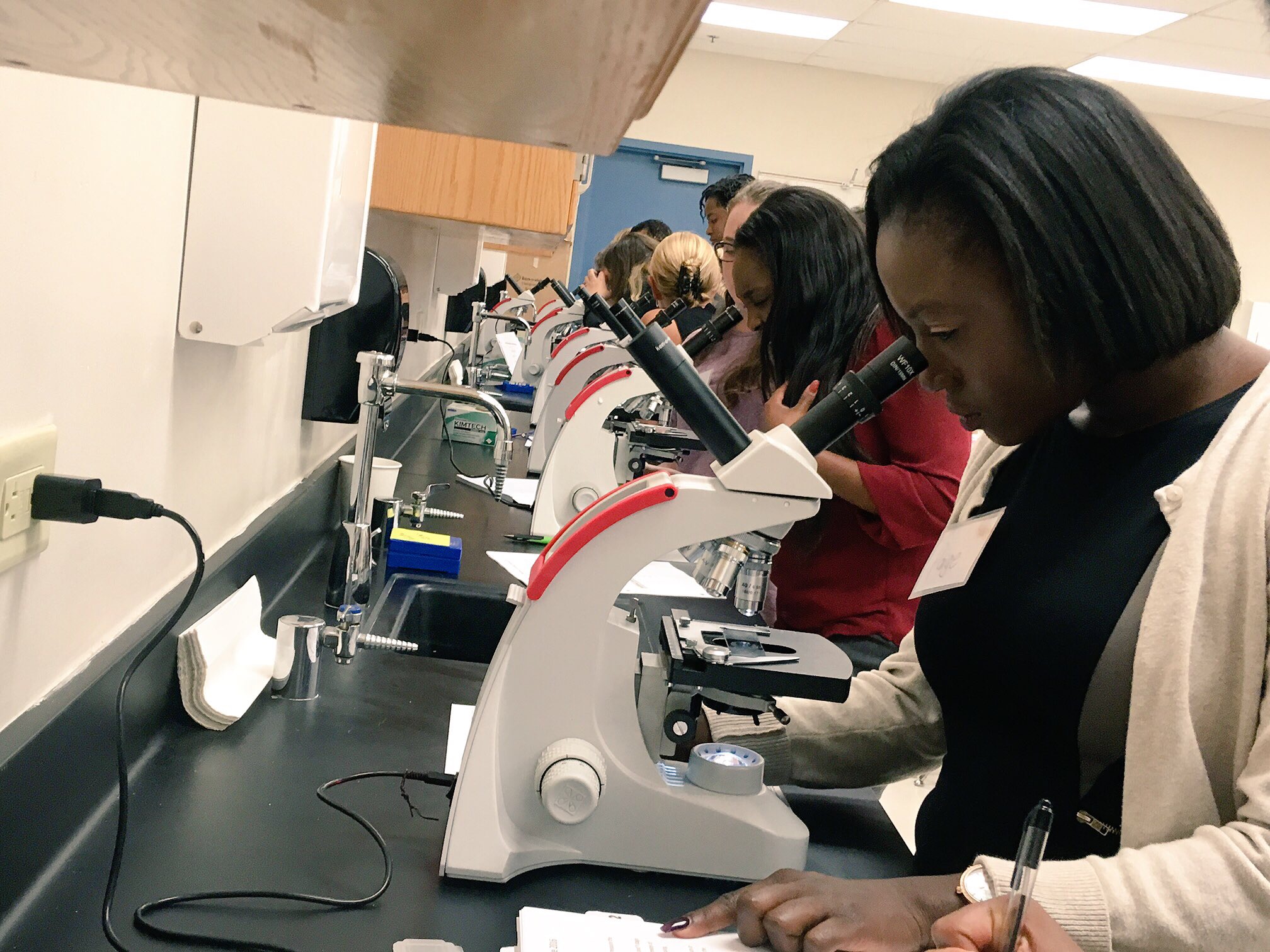 "Photo of a group of people each looking through a microscope."