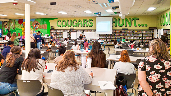 "Large classroom with people looking at a demonstration at the front of the room"