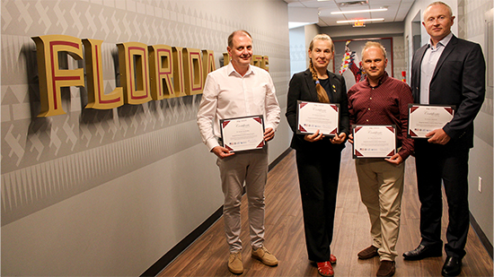 "Four Ukrainian fellows posing with certificates in front of an FSU wall graphic."