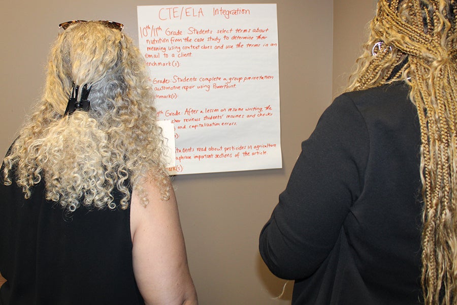 Two women looking at a large sheet of paper on a wall.