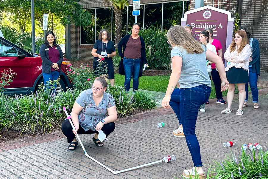 "Two women outside launching a rocket by creating force by stepping on a plastic bottle attached to a long tube."