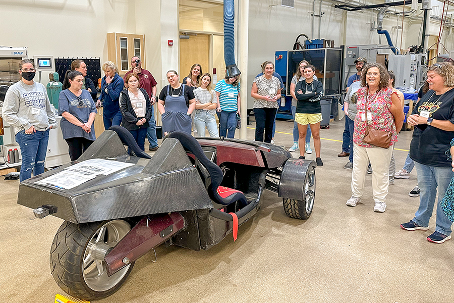 "Group of participants surrounding a futuristic looking vehicle at the High Performance Materials lab."