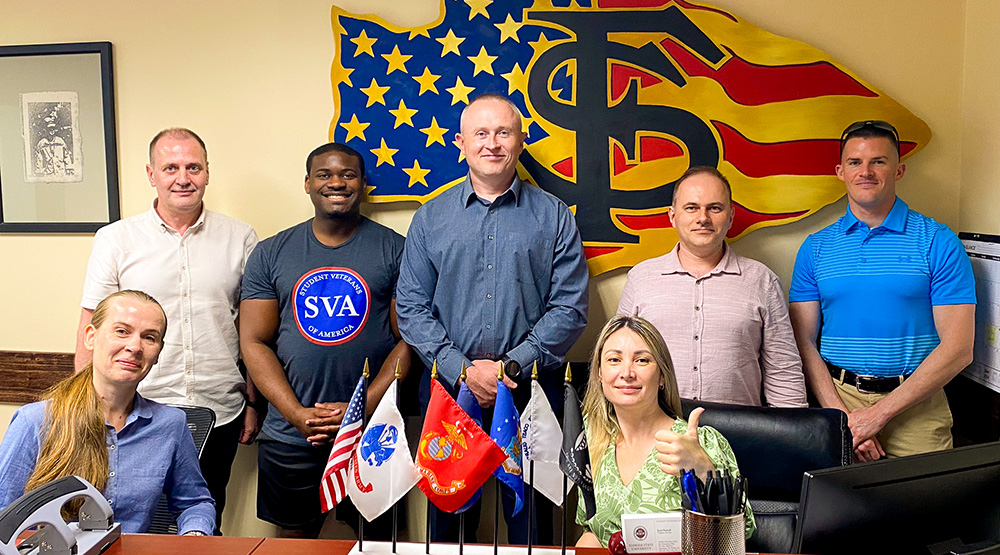 "Ukrainian group poses with Student Veteran Center staff in front of the American flag SVC logo."
