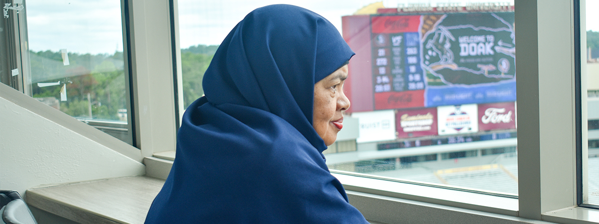 "Dr. Ely Djulia Katmadihardja sitting in front of a giant video board inside the FSU football stadium."