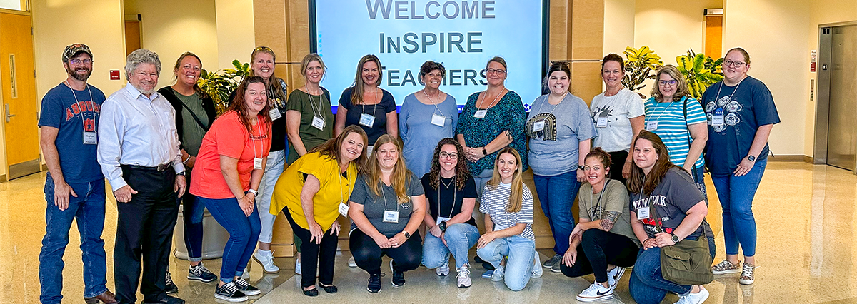 Group photo of instructors at an AI workshop posing in front of a screen with a message welcoming them.
