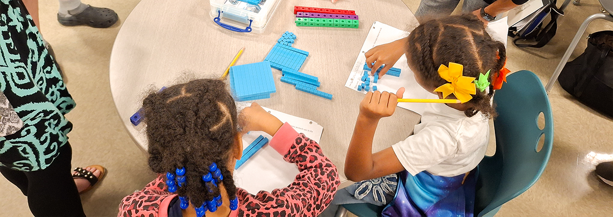 Two young students working at a table on a math problem.