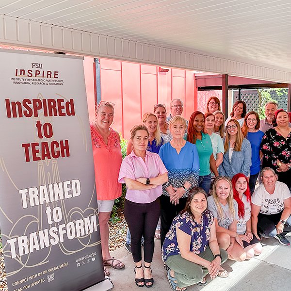Group photo of participants in the FSU InSPIRE summer teacher workshops posing next to a stand-up banner. 