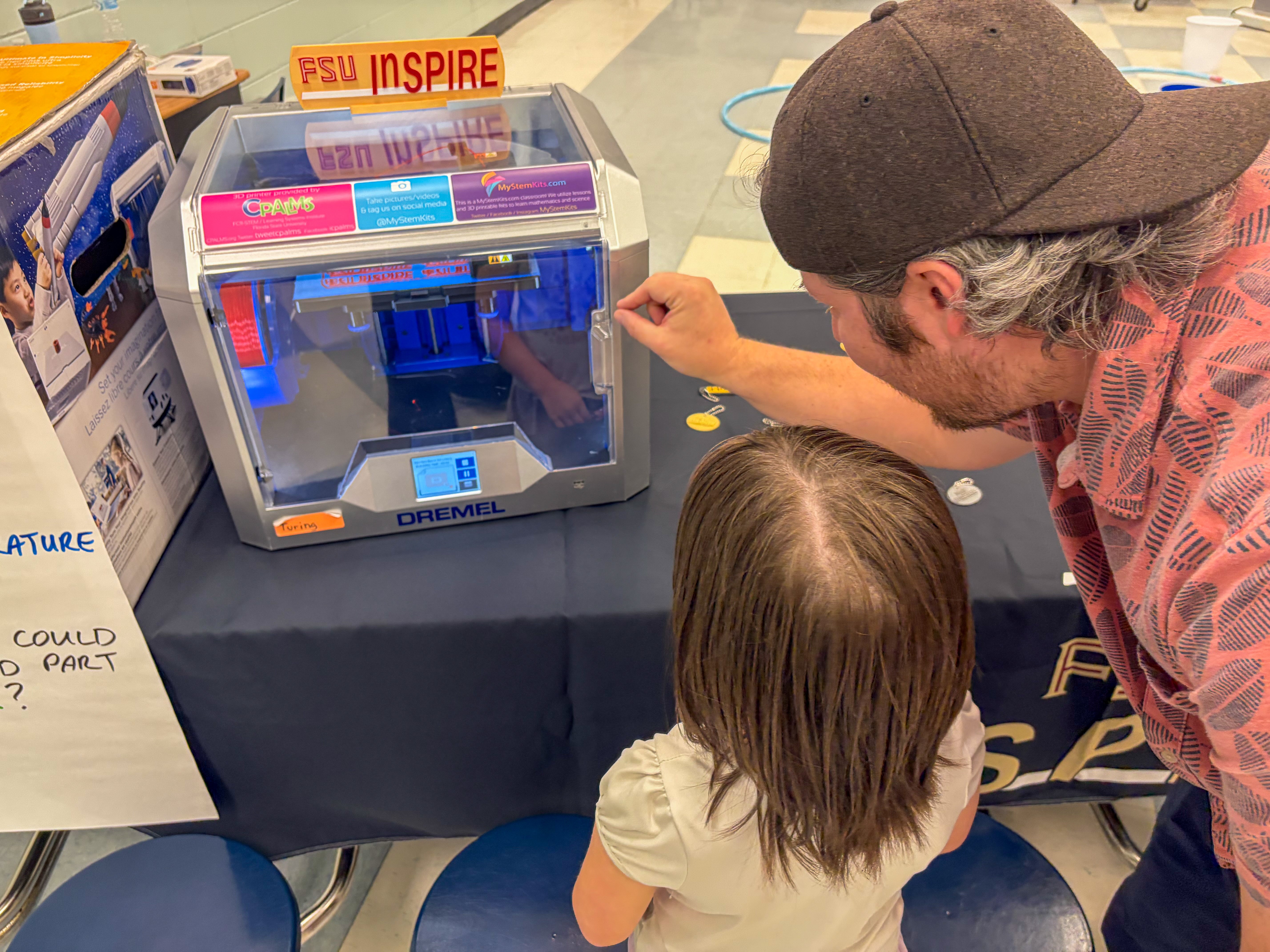 A man and child are watching a 3D printer at a STEM night event. 