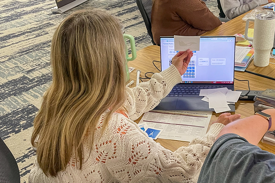 A person sitting at a table in front of a laptop, holding an airplane photo. 