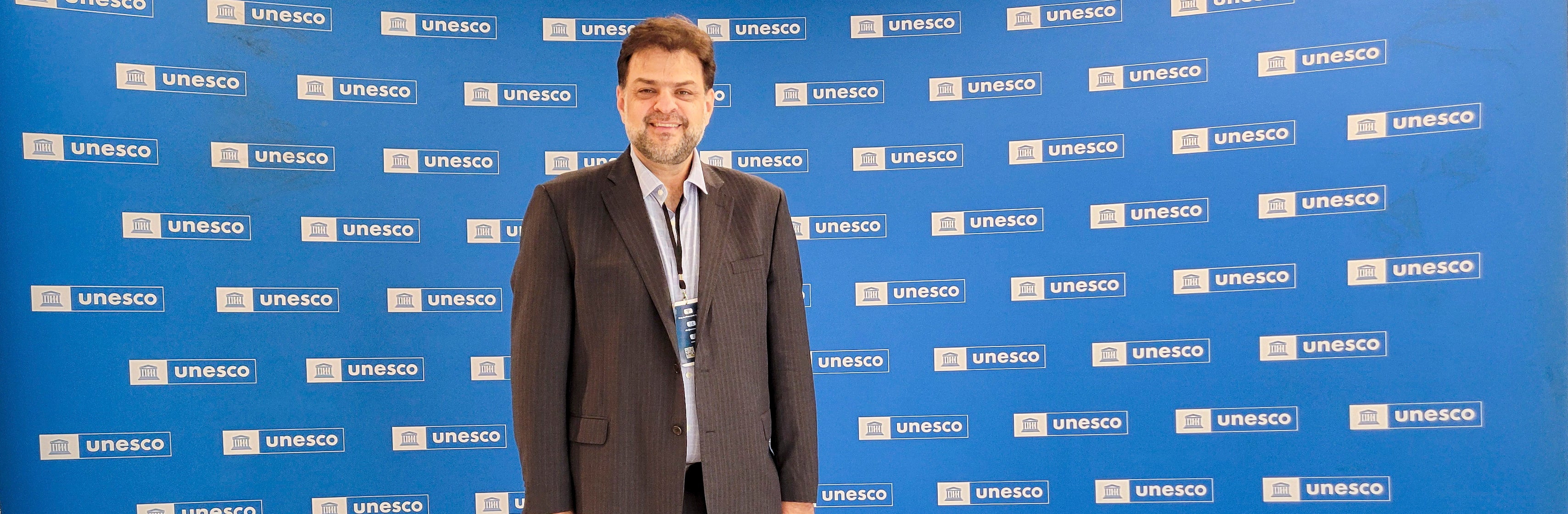 Rabieh Razzouk posing for a photo in front of a large, blue, UNESCO backdrop.