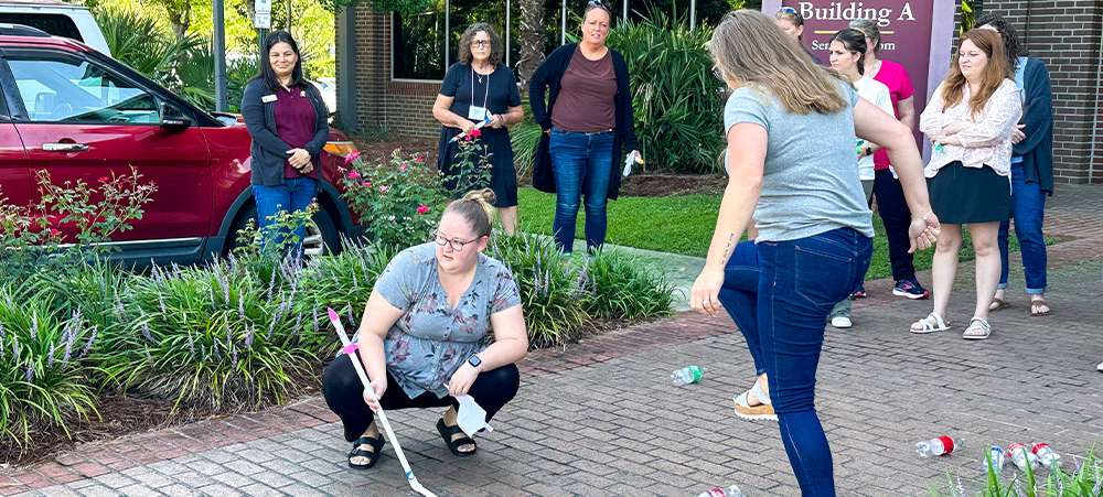 Two participants in the teacher AI workshop outside an FSU building. One is getting ready to launching a small toy rocket by stomping on the end of a tube.