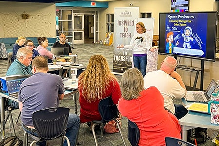 Woman presenting to a room of educators in front of a panel TV screen.