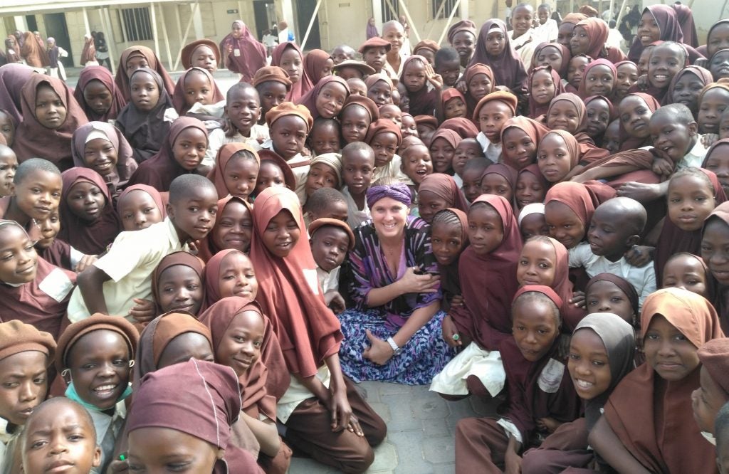 Dr. Adrienne Barnes-Story sitting on the ground surrounded by a group of young children in Nigeria.