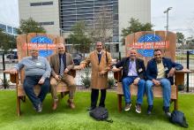 Five men. Two sets of two are sitting in oversized Adarondak chairs