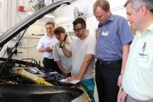 One of the presenters holding a flashlight and examining a car engine