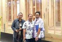 Three men posing in front of the frame of a house