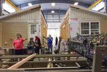 A small group in a classroom posing next to a prefabricated house 