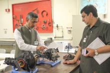 Two men standing around some machine parts