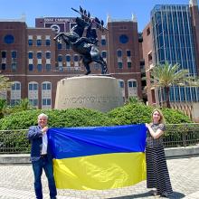 Dr. Paziuk and Dr. Romanova pose with a Ukrainian flag in front of the Unconquered statute on the FSU campus.