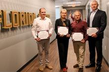Four Ukrainian fellows posing with certificates in front of an FSU wall graphic.