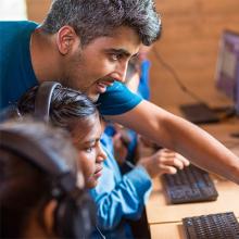 Bhushan Dahal working with children in front of a computer screen.