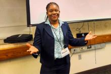 Dr. Brenda Wawire at a conference posing in front of a screen showing her presentation title. 