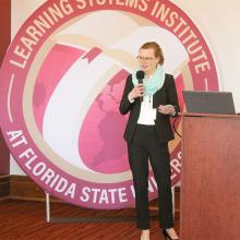 Celia Reddick addressing the LSI staff in front of a large round LSI logo banner.