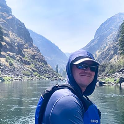 Dr. Rob Schoen posing for a photo in a boat on a lake with mountains behind him.