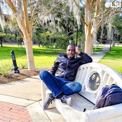 Photo of Bodunrin Akinrinmade sitting on a bench under a tree on the FSU campus.