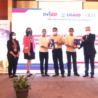 Photo of official materials hand over with a group of people on a stage holding two books wrapped with ribbons.