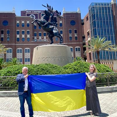 Dr. Paziuk and Dr. Romanova pose with a Ukrainian flag in front of the Unconquered statute on the FSU campus.