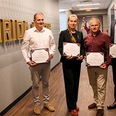 Four Ukrainian fellows posing with certificates in front of an FSU wall graphic.
