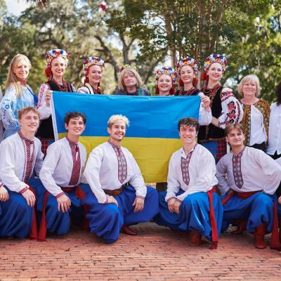 Group photo of people wearing vyshyvankas posing around a Ukrainian flag. 
