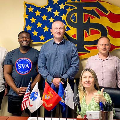 Ukrainian group poses with Student Veteran Center staff in front of the American flag SVC logo.
