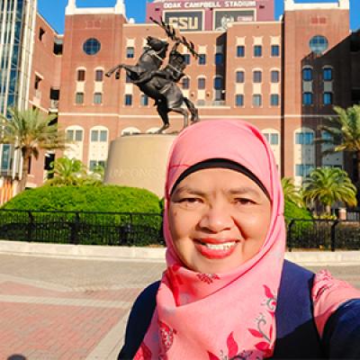 Dr. Ely Djulia Katmadihardja takes a photo in front of the Unconquered Statue on the campus of FSU in front of the football stadium.