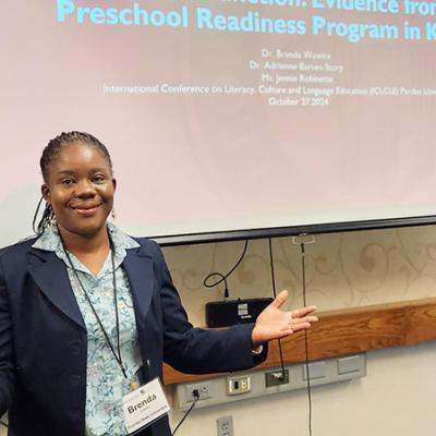 Brenda Wawire posing in front of a projection screen at a conference.