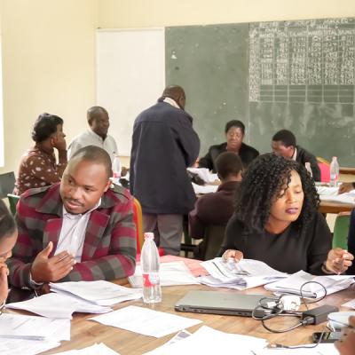 Teacher training in a room with people sitting around tables in discussion.