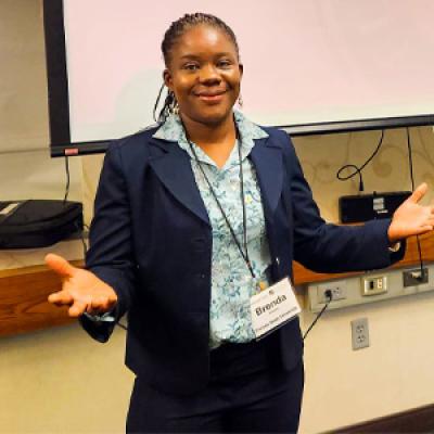 Dr. Brenda Wawire at a conference posing in front of a screen showing her presentation title. 