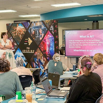 LSI's Carrie Meyers conducting an AI in education session standing next to a flat screen TV.
