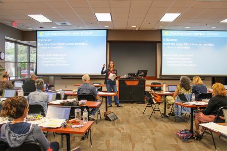 Julie Chappelle instructing in a room of teachers in front of two large projection screens.