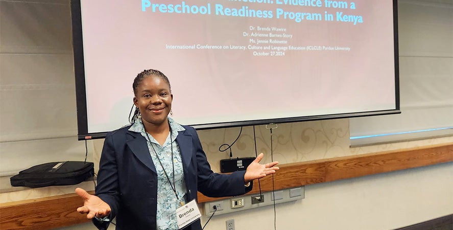 "Brenda Wawire posing in front of a projection screen at a conference."