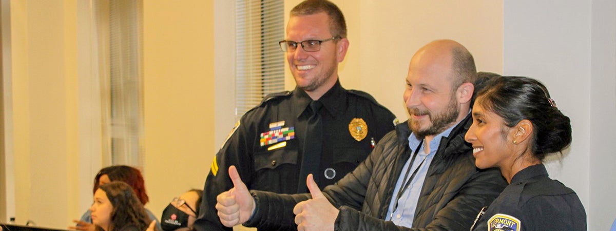 "HECD participant GIVING TWO THUMBS UP WHILE POSING WITH POLICE OFFICERS."